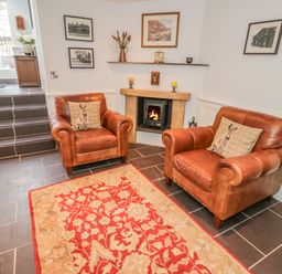 A sitting area with two brown leather armchairs facing a fireplace and a red patterned rug on a tiled floor at Bryn Derwen Coach House in Bethesda