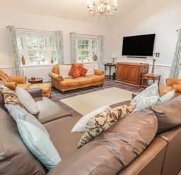 A living room with multiple leather sofas facing a wall mounted television at Bryn Derwen Coach House in Bethesda