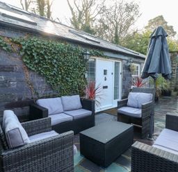 An outdoor patio with rattan furniture and cushions in front of a stone wall with ivy at Bryn Derwen Coach House in Bethesda