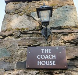 A stone wall with a lantern and a sign that reads The Coach House at Bryn Derwen Coach House in Bethesda