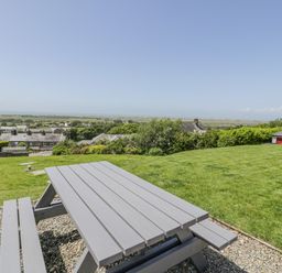 A picnic table on a gravel area with green lawn and houses in the background at Bryn Coch Bach in Dyffryn Ardudwy