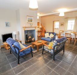 A living room with blue sofas, a wooden coffee table, a wood stove, a dining table with chairs, and a television at 8 Lios Na Sioga in Binghamstown near Belmullet County Mayo