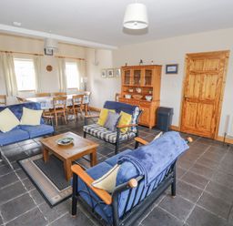 A living room with blue sofas a wooden coffee table a dining table and chairs and a wooden cabinet at 8 Lios Na Sioga in Binghamstown near Belmullet County Mayo