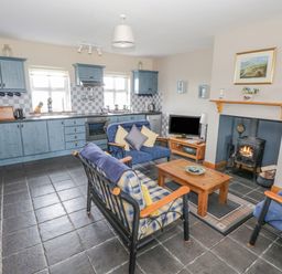 A kitchen and living area with blue cabinets wood stove television and seating at 8 Lios Na Sioga in Binghamstown near Belmullet County Mayo