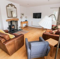 A living room with two brown leather sofas a gray armchair a fireplace a wall mirror a wooden side table and a wall-mounted TV at Llety'r Llwynog in Llanfallteg near Narberth