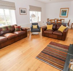 A living room with two brown leather sofas a grey armchair a wooden dining table with chairs and a striped rug at Llety'r Llwynog Llanfallteg near Narberth