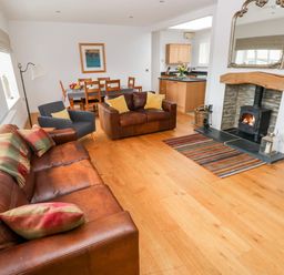 A living room with leather sofas and a wood stove fireplace at Llety'r Llwynog in Llanfallteg near Narberth