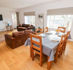 A dining area with a table set for six next to a living space with two brown leather sofas and a wall-mounted TV at Llety'r Llwynog in Llanfallteg near Narberth