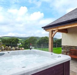 An outdoor hot tub next to a wooden bench with a stone wall and countryside view at Tyn Y Celyn Uchaf in Clocaenog near Ruthin