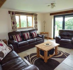 A living room with leather sofas a wooden coffee table and large windows at Tyn Y Celyn Uchaf Clocaenog near Ruthin
