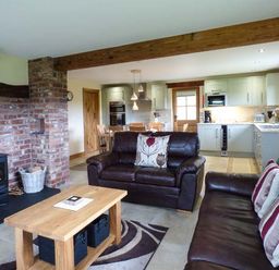 An open living room and kitchen with leather sofas wooden coffee table and brick fireplace at Tyn Y Celyn Uchaf in Clocaenog near Ruthin