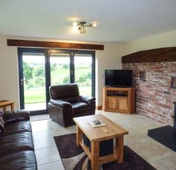 A living room with leather sofas a wooden coffee table a wood stove and a television with glass doors showing outside at Tyn Y Celyn Uchaf in Clocaenog near Ruthin
