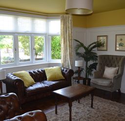 A sitting room with leather sofas, an armchair, a wooden coffee table, lamps, framed pictures, and a large window at Lily House in Minehead