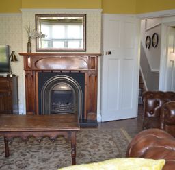 A living room with a wooden fireplace centered below a mirror and a wooden table in front at Lily House in Minehead