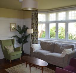 A living room with a large window a gray sofa a green armchair a purple chair and a wooden coffee table at Lily House in Minehead