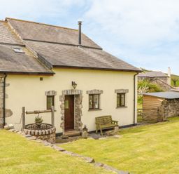 A stone and cream colored house with a wooden door stone framed windows a wooden bench and a stone well in a grass yard at Higher Whiddon Farm Whiddon Well Ashburton near Newton Abbot
