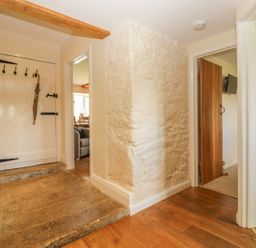 A hallway with wooden floors a white wooden door and two doorways leading to other rooms at Higher Whiddon Farm Whiddon Well Ashburton near Newton Abbot