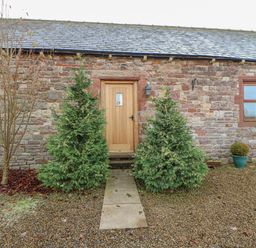 A stone building with wooden door and window with a pathway and shrubs at Swift Cottage in Milton near Brampton