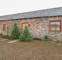 A stone building with a wooden door two windows and small trees in front at Swift Cottage in Milton near Brampton