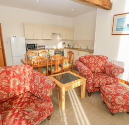 A living area with two patterned armchairs and an ottoman a wooden coffee table and a dining table with chairs in a kitchen at Swift Cottage in Milton near Brampton