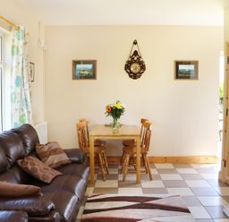 A living room with a brown leather sofa pillows a wooden dining table with four chairs and a vase of flowers on it at Clash-Brack in Dungarvan County Waterford