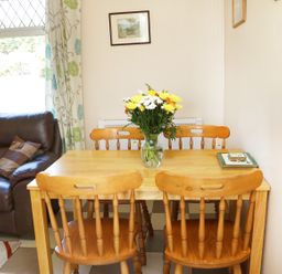 A wooden dining table with four chairs and a vase of flowers next to a brown leather sofa with cushions at Clash-Brack in Dungarvan County Waterford