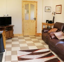 A living room with brown leather sofas a patterned rug a wooden door and a television at Clash-Brack in Dungarvan County Waterford