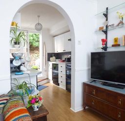A living room with a colorful striped blanket on a sofa a wooden cabinet with a television and shelves with books and decor at Tidewood in Polzeath