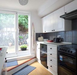 A kitchen with white cabinets black appliances and glass doors leading outside at Tidewood in Polzeath