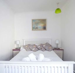 A bedroom with a white bed framed by two bedside tables with lamps and a painting on the wall at Tidewood in Polzeath