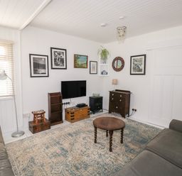 A living room with two sofas a round wooden table and a wall mounted TV at Driftwood in Polzeath near Wadebridge