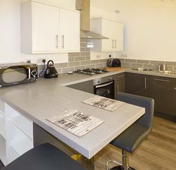 A kitchen with a microwave kettle and toaster on the counter and bar stools at White Cottage Annexe Tenby
