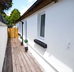 A narrow outdoor walkway with wood decking and white walls on both sides at White Cottage Annexe in Tenby