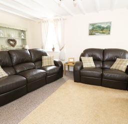 A living room with two brown leather sofas a beige rug a side table with a frame and a basket with firewood at Penglanowen Fawr in Llangwyryfon near Aberystwyth