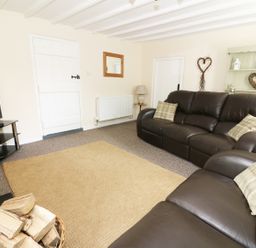 A living room with leather sofas a television a basket of firewood and a rug at Penglanowen Fawr in Llangwyryfon near Aberystwyth
