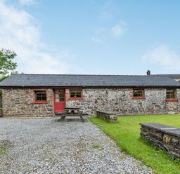 A stone cottage with a slate roof a red door and three windows with a picnic bench on a gravel area and grass at Cilwen Fach in Cynwyl Elfed