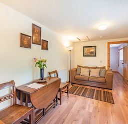 A living room with a brown sofa cushions a wooden dining table with chairs and a floor lamp at Cilwen Fach in Cynwyl Elfed