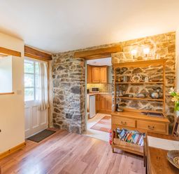 A room with wooden furniture stone walls an entrance door and a view into a kitchen at Cilwen Fach in Cynwyl Elfed