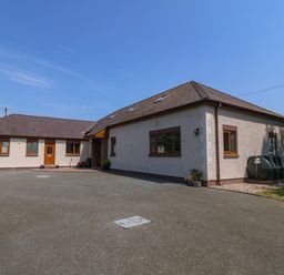 An exterior view of a one-story house with brown roof tiles and several windows with wooden frames at Fferam Y Llyn in Rhosgoch near Cemaes Bay