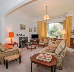 A living room with patterned armchairs, a sofa, wooden tables, a fireplace, and yellow curtains at West Ridge in Boscombe