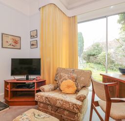 A living room with an armchair and ottoman beside a television on a wooden stand near a sliding glass door overlooking a garden at West Ridge in Boscombe