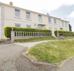 Exterior of a two-story cream-colored building with multiple windows and a hedge-lined stone balustrade in front at Tremanners in St Agnes