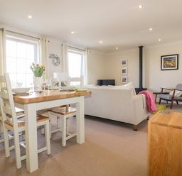 A living room and dining area with a wooden dining table set with plates and glasses and a sofa facing a wood stove at Tremanners in St Agnes