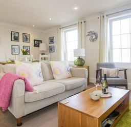 A living room with a beige sofa a pink throw a wooden coffee table and framed pictures on the wall at Tremanners in St Agnes