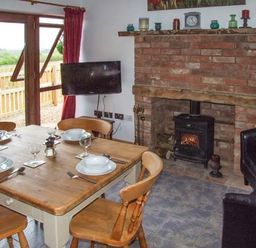 A dining area with a wooden table set for four and a brick fireplace with a stove and a wall-mounted TV at Owl Cottage in Napton-on-the-Hill near Southam