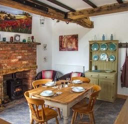 A dining room with a wooden table set for four and a brick fireplace at Owl Cottage in Napton-on-the-Hill near Southam