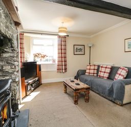 A living room with a stone fireplace a sofa with cushions a wooden coffee table and a television at Duddon Cottage in Broughton-in-Furness