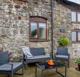 An outdoor patio with black wicker chairs and a table in front of a stone building at The Stables in Llanfair Caereinion near Welshpool