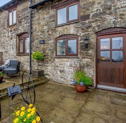 An outdoor stone patio with a wooden door and windows on a stone building at The Stables in Llanfair Caereinion near Welshpool