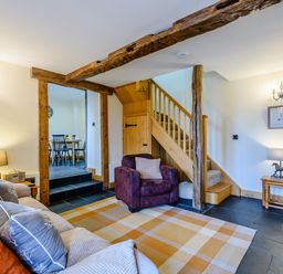A living room with sofa and armchair near stairs and a doorway leading to a dining area at The Stables in Llanfair Caereinion near Welshpool